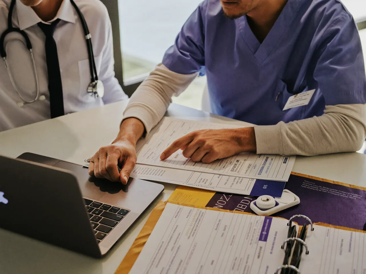 A credentialing specialist and a physician reviewing Medicare and commercial payer enrollment forms